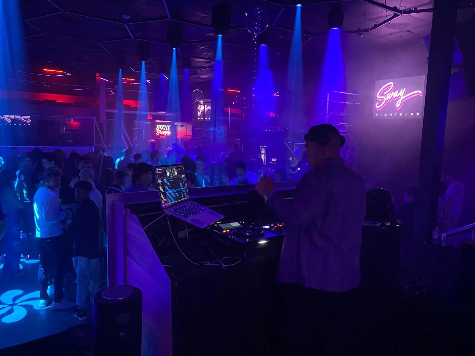 DJ booth in a nightclub with a pink neon sign